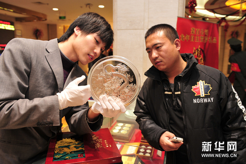 12月21日，工作人员向顾客介绍一款5公斤重的壬辰贺岁纪念大银章，其正面的“金龙降喜”图案，寓意对龙年万事亨通的美好祝福。新华网图片 杨光